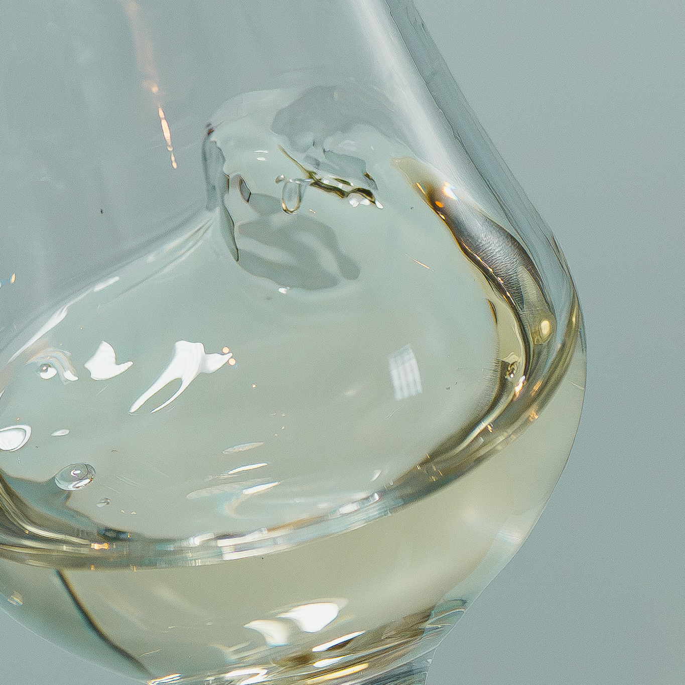 Gros plan sur un verre tulipe en plein mouvement de rotation, créant une ondulation du spiritueux blanc cristallin pour libérer ses arômes lors d'une dégustation - Sainte Harmonie, Baijiu Français.