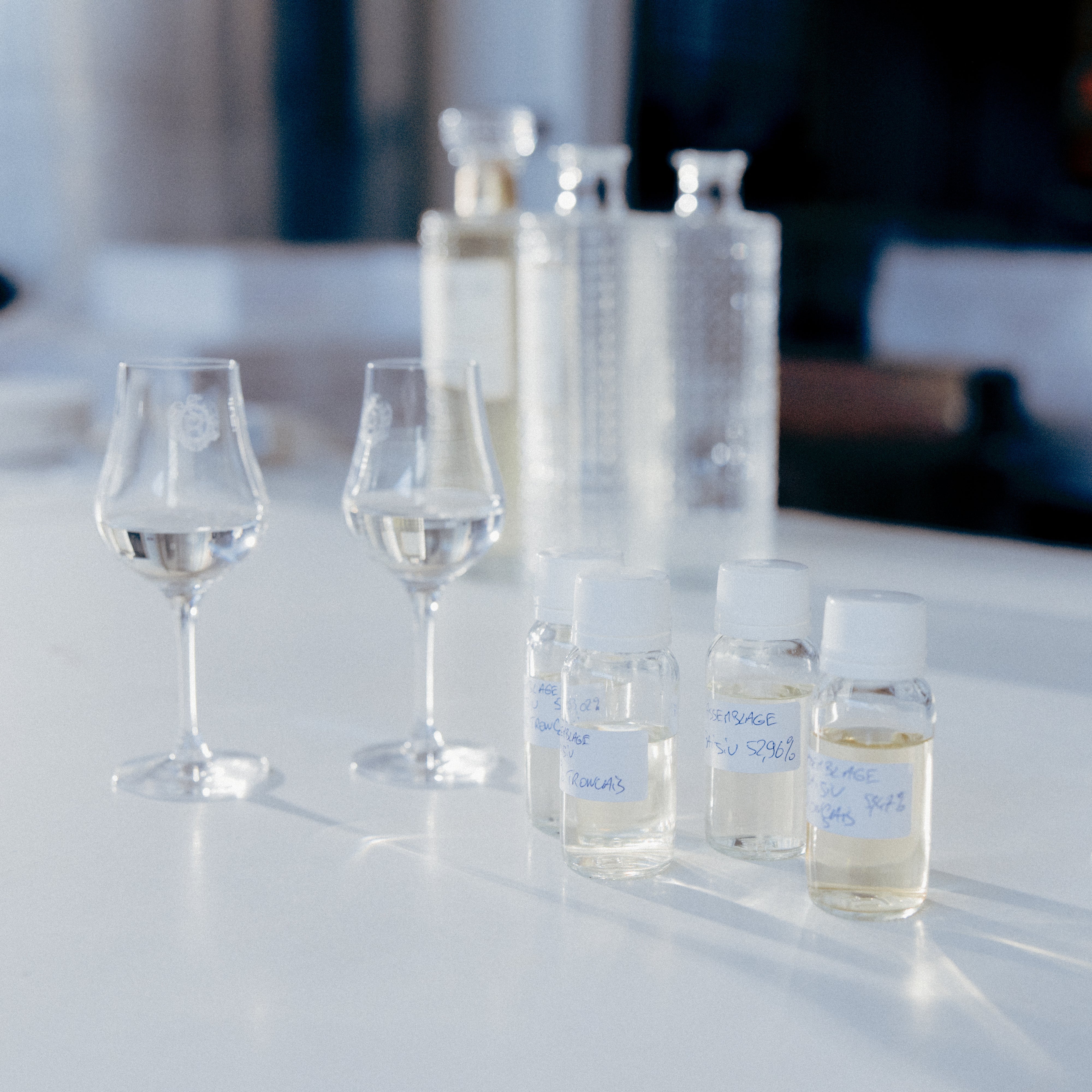 Vue d'une table de travail partagée entre verres de dégustation tulipe et des échantillons de spiritueux pour l'assemblage - Sainte Harmonie, Baijiu Français.